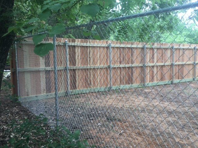 A chain link fence with a wooden fence behind it