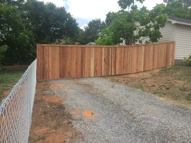 A wooden fence surrounds a gravel driveway next to a chain link fence.