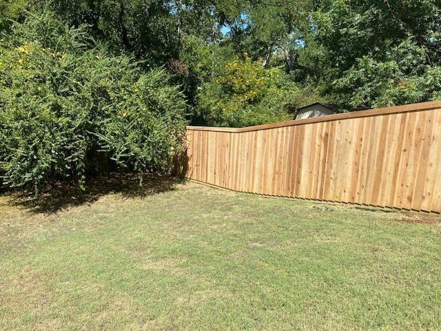 A wooden fence is surrounded by trees in a backyard.