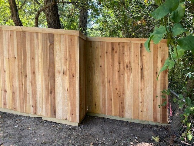 A wooden fence is sitting on top of a dirt field next to trees.