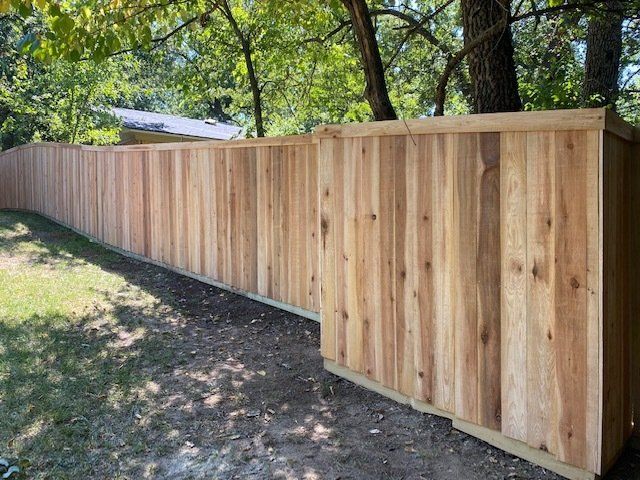 A long wooden fence is surrounded by trees in a backyard.