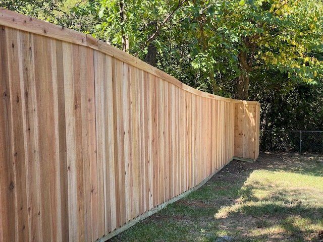 A wooden fence in a backyard with trees in the background.