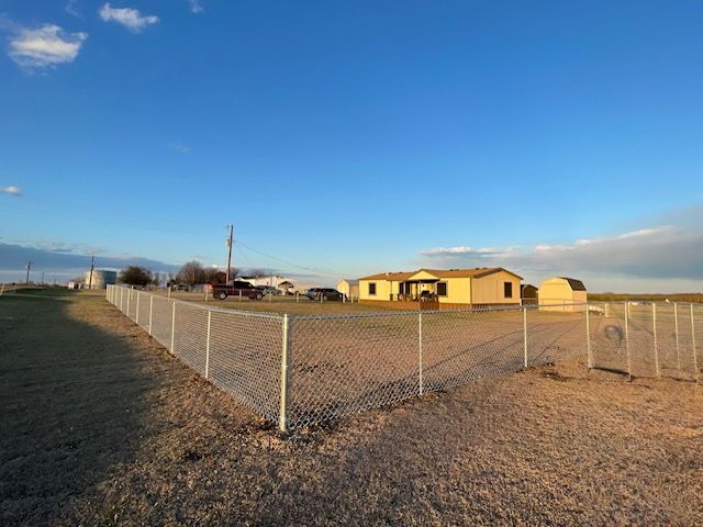 A chain link fence surrounds a dirt field with a house in the background.