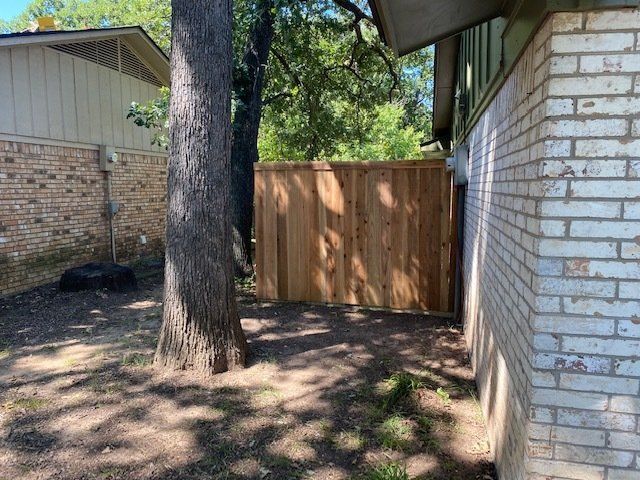 A wooden fence is in the backyard of a brick house.