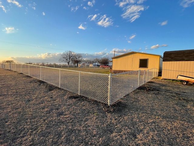 A chain link fence is surrounding a dirt field with a shed in the background.