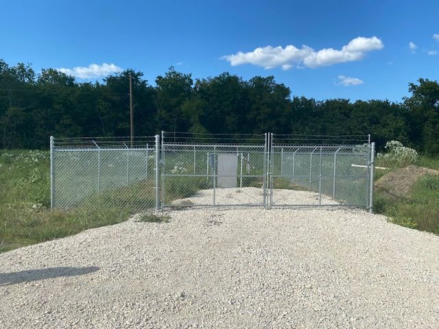 A chain link fence with a gate in the middle of a gravel road.