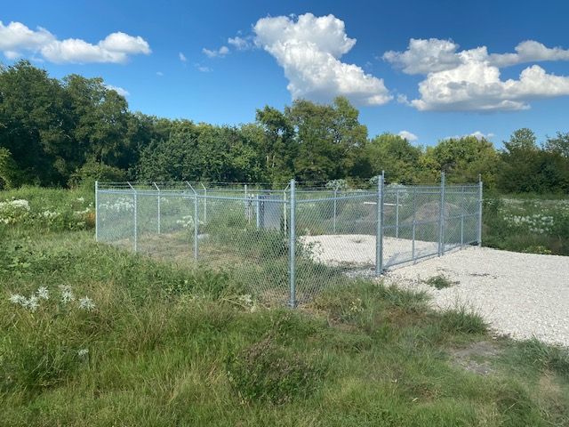 A chain link fence surrounds a grassy field with trees in the background