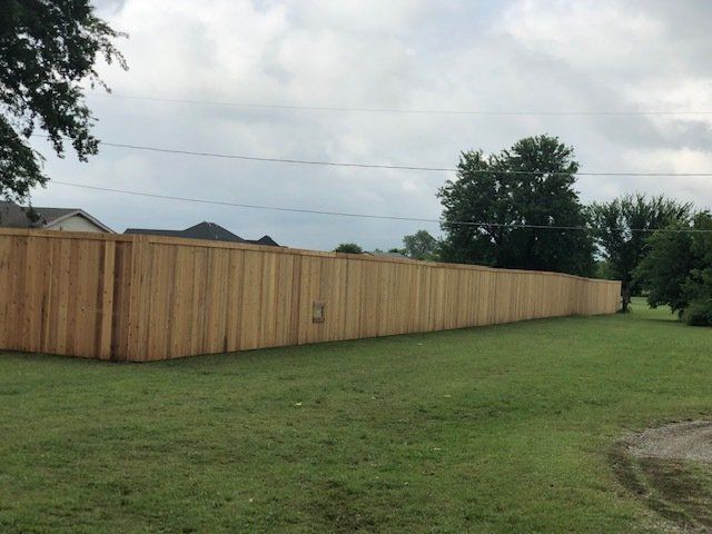 A long wooden fence surrounds a lush green field.