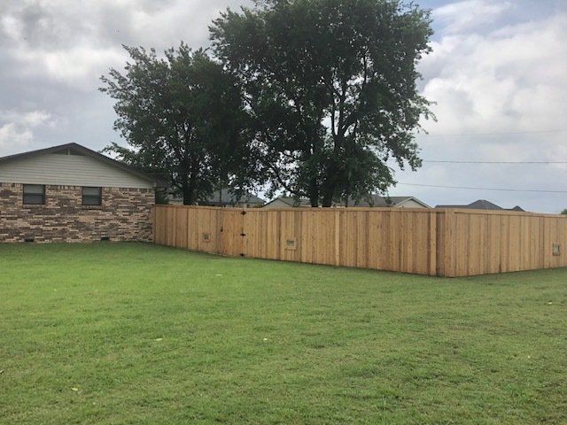 A wooden fence surrounds a lush green yard in front of a house.