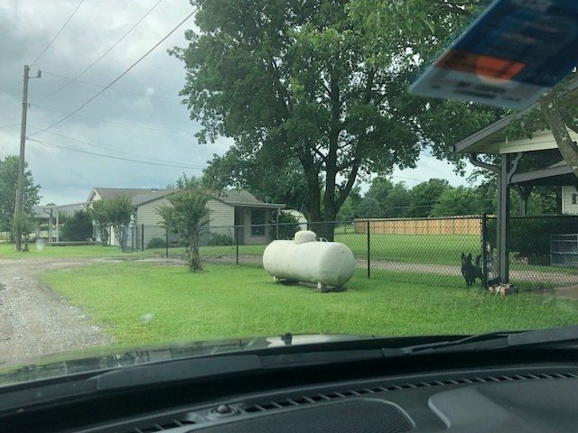 A propane tank is sitting in the grass in front of a house.