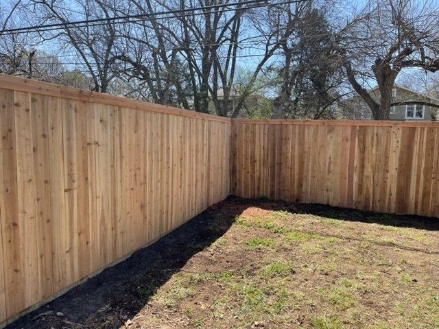 A wooden fence in a backyard with trees in the background.