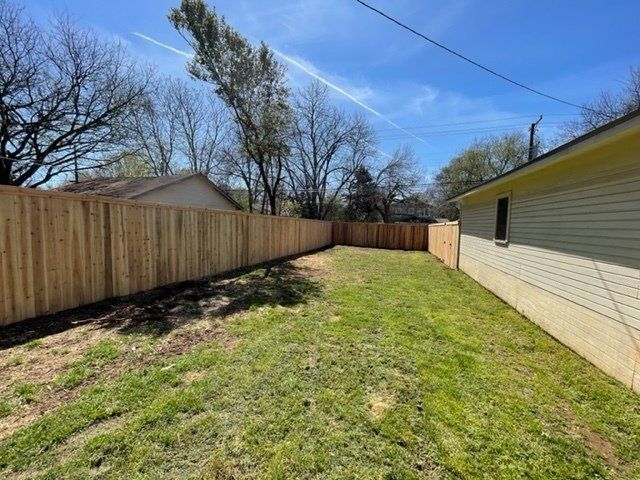 A backyard with a wooden fence and a house in the background.