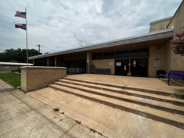 A large building with stairs leading up to it and a purple bench in front of it.