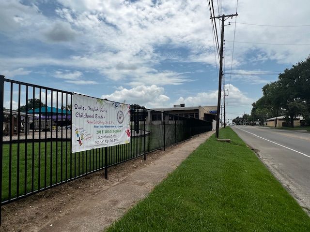 A sign is hanging on a fence next to a road.