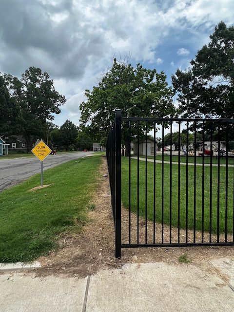 A black fence surrounds a grassy area with a yellow sign that says do not enter