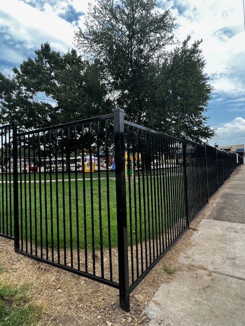 A black fence surrounds a park with trees in the background