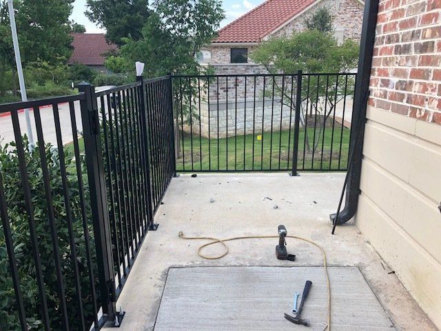 A black fence is being installed on a sidewalk next to a brick building.