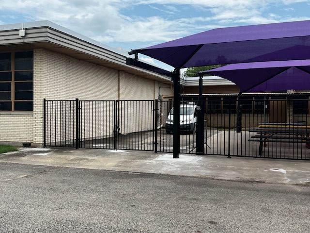 A car is parked under a purple umbrella in front of a building
