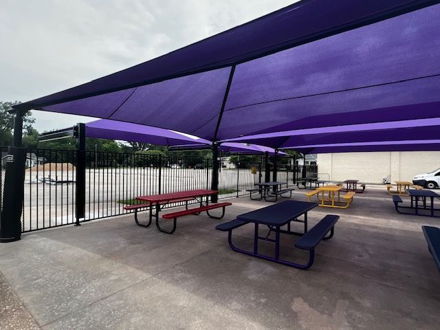 A lot of picnic tables under purple umbrellas