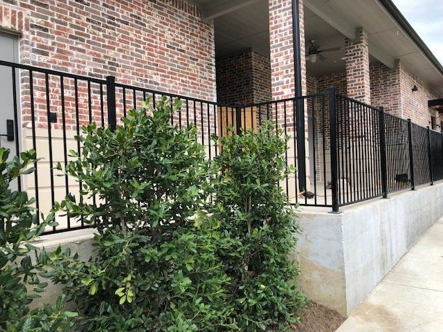 A brick house with a black fence and bushes in front of it.