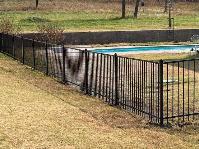 A black fence surrounds a swimming pool in a backyard.