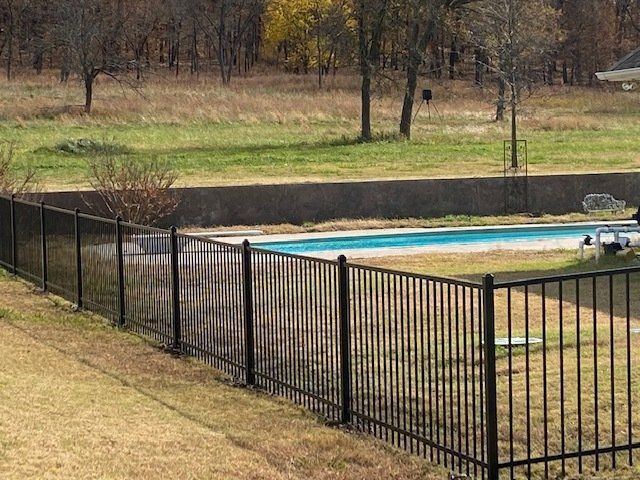 A black fence surrounds a swimming pool in a backyard.