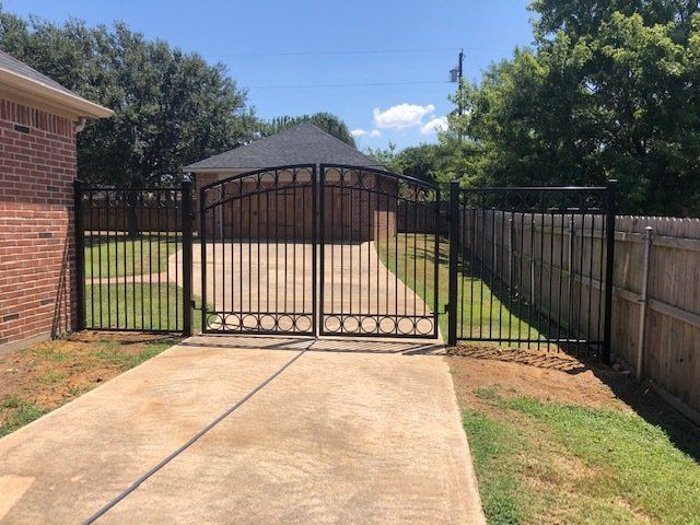 A black wrought iron gate is surrounding a driveway leading to a house.