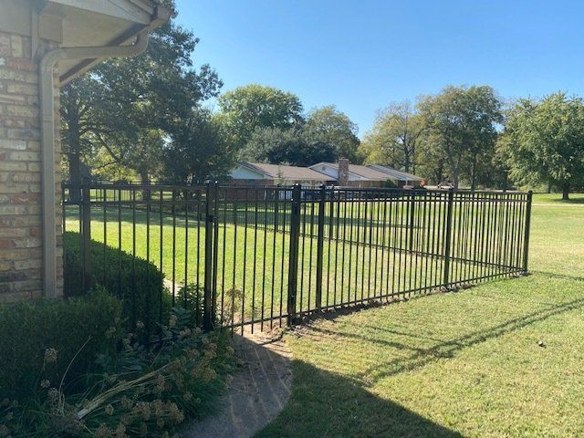 A black metal fence surrounds a lush green yard in front of a house.