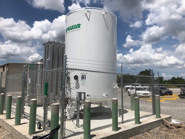 A large white tank is surrounded by green poles and a chain link fence.