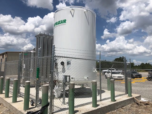 A large white tank is surrounded by green poles and a chain link fence.
