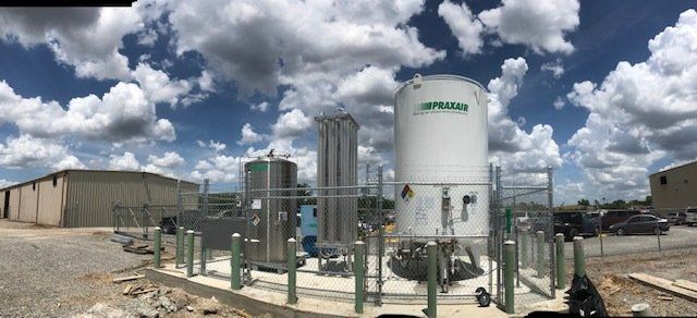 A large white tank is sitting in a fenced in area in front of a building.