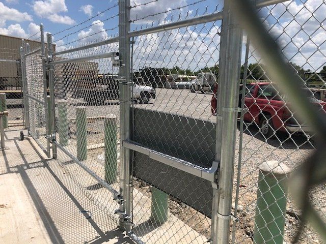 A chain link fence is surrounding a parking lot with a red truck parked in the background.