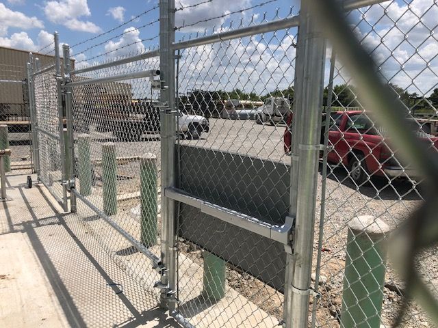 A chain link fence is surrounding a parking lot with a red truck parked in the background.