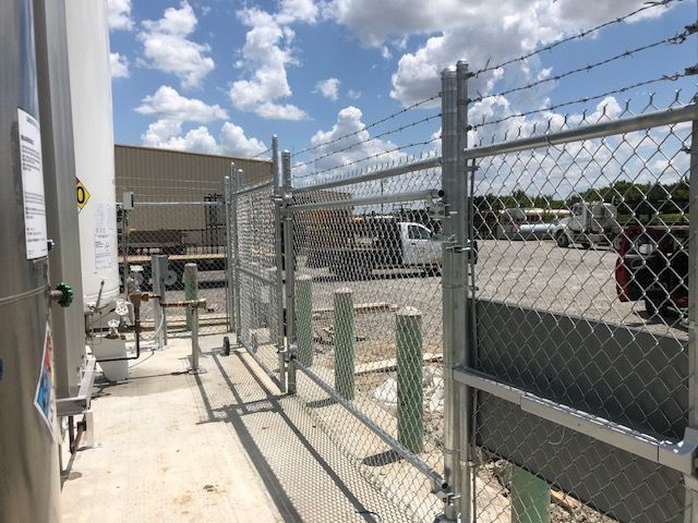 A chain link fence with barbed wire surrounding a parking lot.