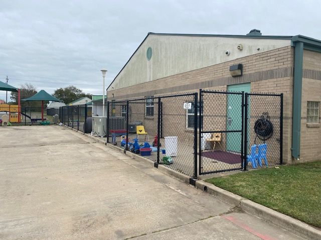 A chain link fence surrounds a brick building with a playground in front of it.