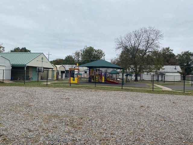A playground with a green umbrella in front of a building.