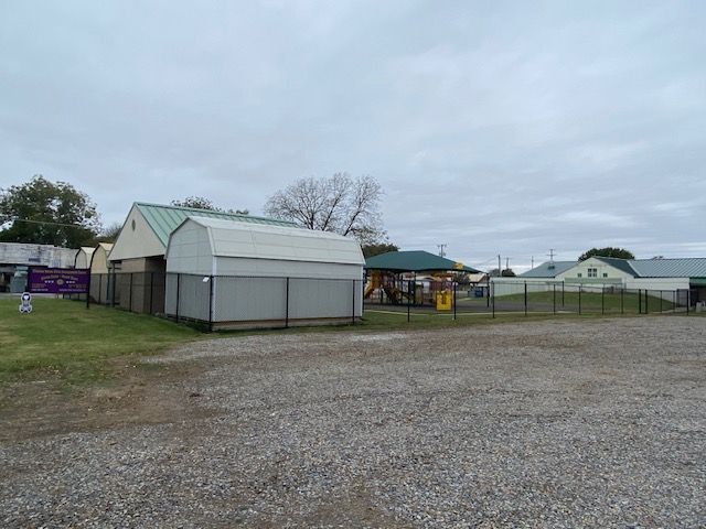 A fenced in area with a shed and a playground in the background