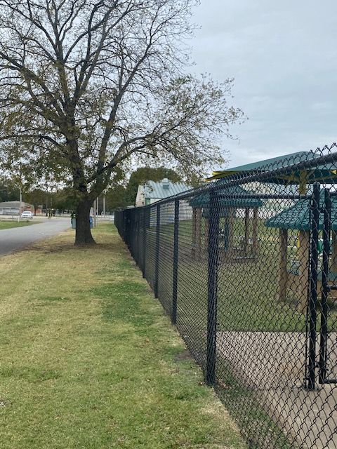 A chain link fence surrounds a picnic area in a park.