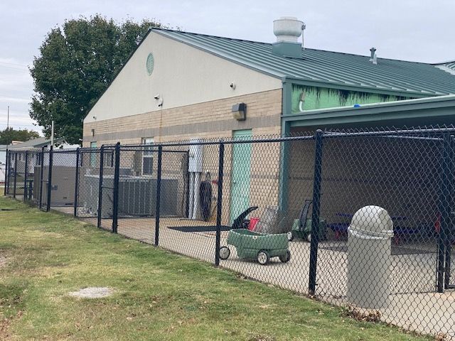 A chain link fence surrounds a building with a green wagon in front of it.