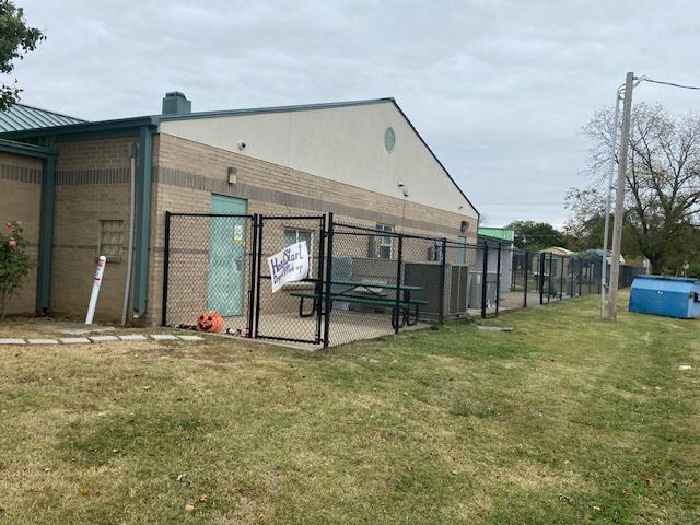 A building with a fence around it and a picnic table in front of it.
