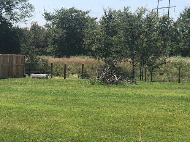 A large lush green field with a fence and trees in the background.