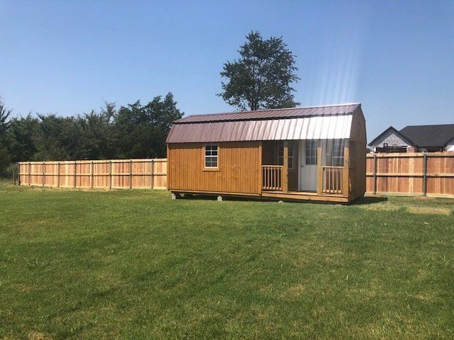 A small wooden shed is sitting in the middle of a lush green field.