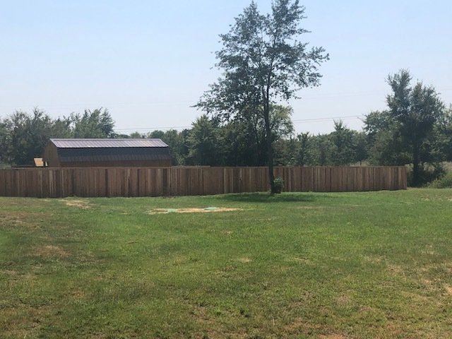 A large grassy field with a wooden fence and a shed in the background.