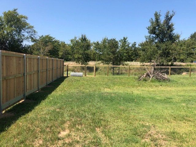 A wooden fence surrounds a grassy field with trees in the background.