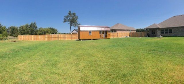 A large lawn with a wooden fence and a house in the background.