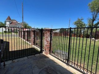 A black metal fence surrounds a brick wall in a yard.