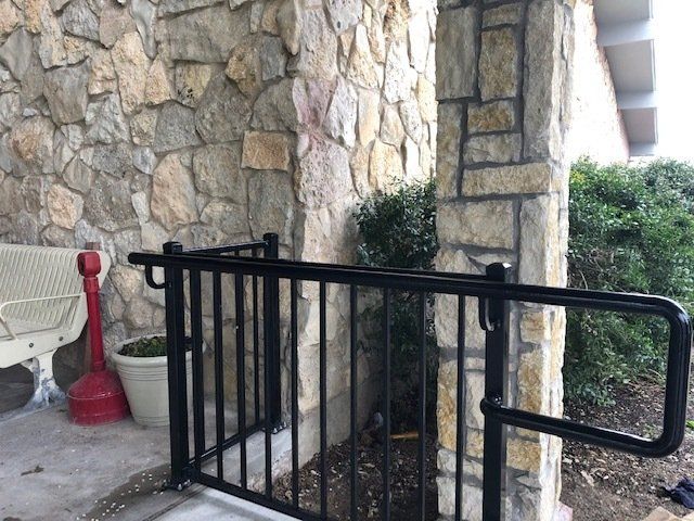 A black railing is sitting in front of a stone wall.