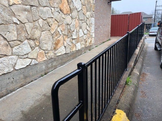 A black fence along a sidewalk next to a stone wall