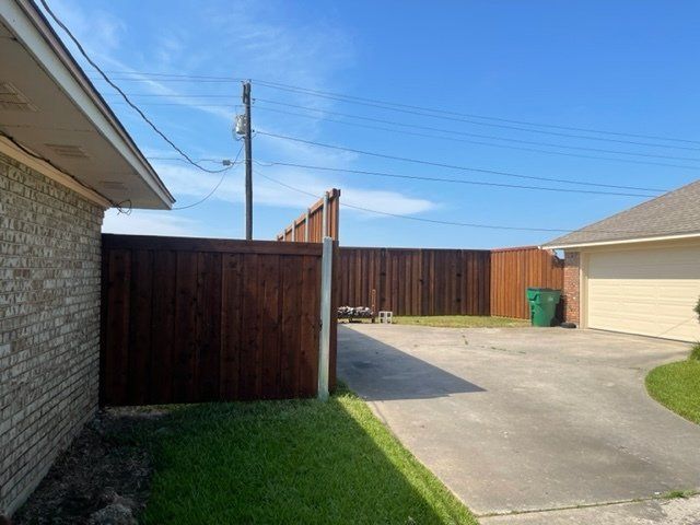 A wooden fence surrounds a driveway between two houses.