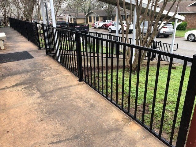 A black metal fence along a sidewalk with cars parked behind it.